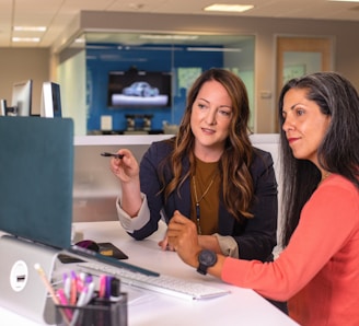 two women sitting at a table looking at a computer screen