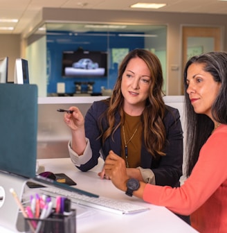 two women sitting at a table looking at a computer screen