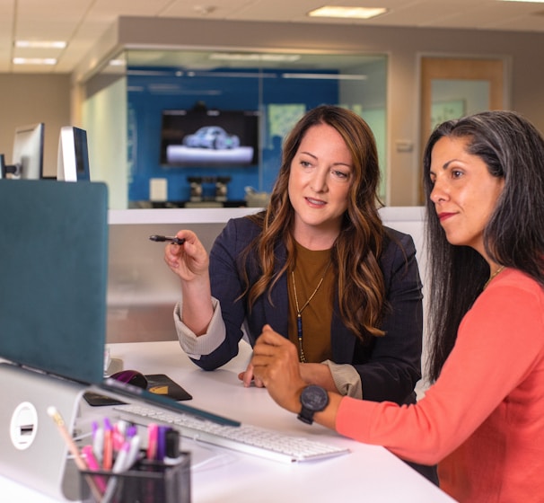 two women sitting at a table looking at a computer screen
